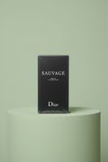 Hand holding a Dior Sauvage packaging against a light green background